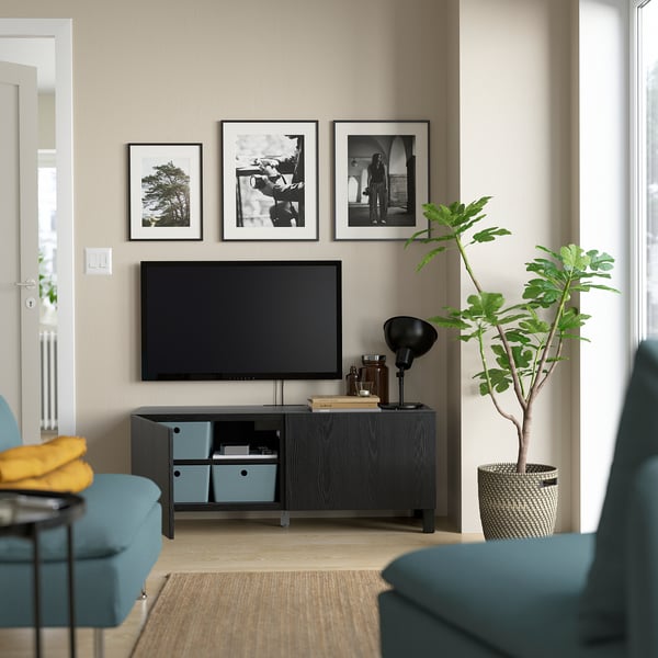 Salon moderne avec télévision à écran plat, poubelles bleues, lampe, plante et photos en noir et blanc
