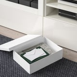 Boîte TJENA blanche ouverte contenant des cahiers et de la papeterie, idéale pour l’organisation du bureau.