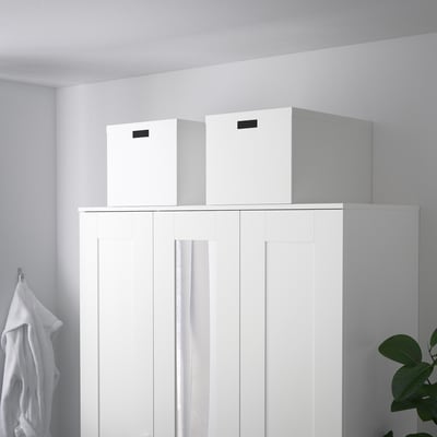 Deux boîtes de rangement TJENA sur armoire blanche, robustes, recyclées, avec poignées découpées.