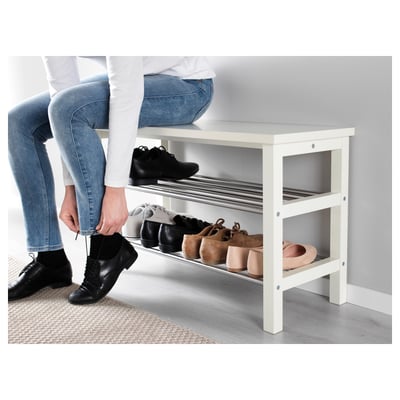 Description de l’image : personne enfilant des chaussures noires, à l’aide d’un porte-chaussures TJUSIG. Chaussures rangées sur les étagères supérieures et inférieures.