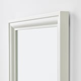 Miroir encadré blanc avec des bords simples et nets. Monté verticalement sur un mur uni.
