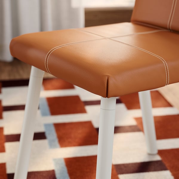 Tabouret marron, pieds blancs, coutures, tapis à motifs.