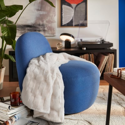 Chaise TORPSPIREA bleue douillette avec une couverture blanche douce, à côté des disques et de la plante.