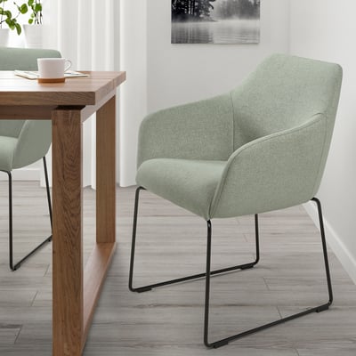 Chaise TOSSBERG moderne avec rembourrage vert, pieds noirs. Minimaliste, sous une table en bois avec une tasse et une serviette. 148 caractères