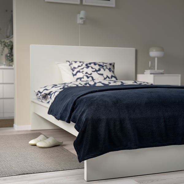 Chambre moderne Couvre-lit polaire gris foncé TRATTVIVA sur lit blanc, plus grand que des pantoufles, avec un design d’oreiller abstrait.