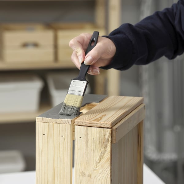 Personne peignant des meubles en bois avec un pinceau noir.