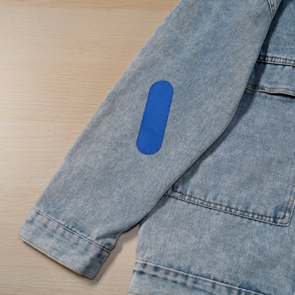 Le kit de réparation de tissu gris comprend de petits ciseaux, des épingles, des fils et des patchs. Tache bleue visible sur un tissu gris, indiquant un processus de réparation facile.