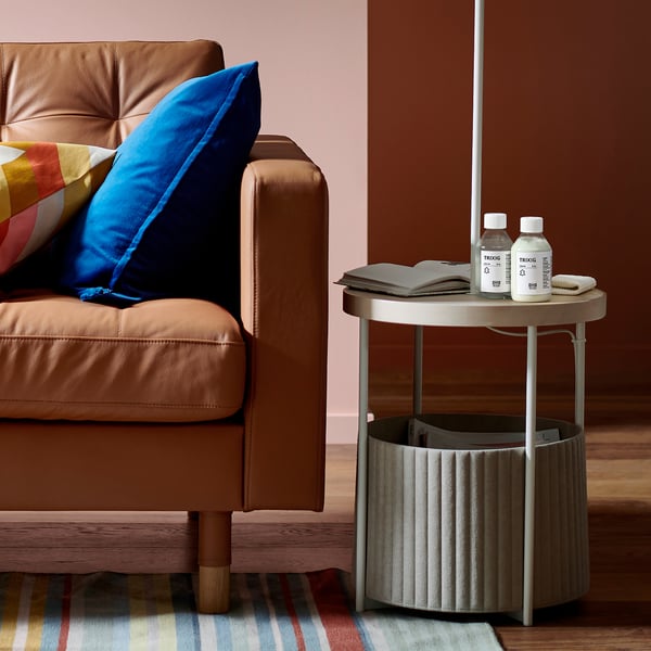 Canapé en cuir avec oreillers bleus, bouteilles de nettoyant sur la table d’appoint, lampe, tapis rayé.