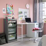 Armoire grise TROFAST avec tiroirs en maille à côté d’un bureau et d’une chaise blancs, idéale pour la chambre d’adolescent avec de nombreux rangements.