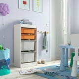 Chambre d’enfant avec meuble de rangement TROFAST blanc, bacs orange et gris, livres et table bleue.