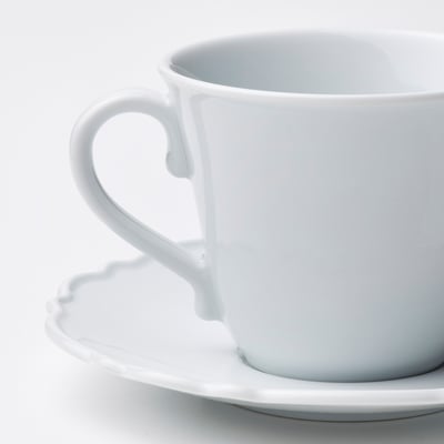 Quatre tasses et soucoupes en porcelaine blanche aux bords volantés, soigneusement disposées sur un fond blanc.