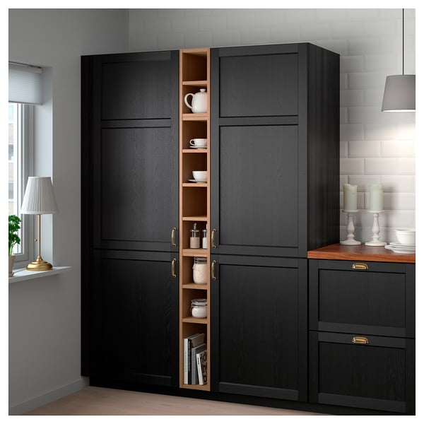 Armoire de rangement noire VADHOLMA en bois foncé et compartiment ouvert contre mur blanc, éclairé par une lampe.