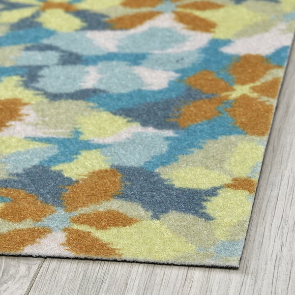 Tapis abstrait aux couleurs vives, posé sur un plancher en bois. Texture douce, motifs complexes visibles.
