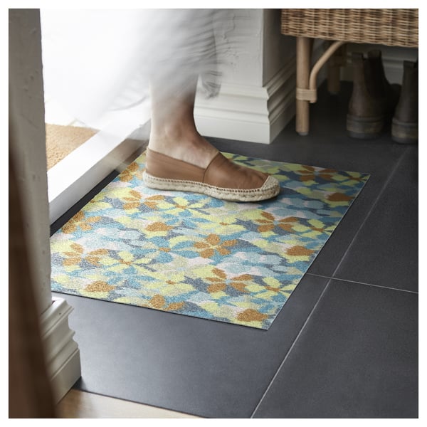 Montez sur un tapis VÄLFÄRD, doté d’un motif floral bleu, vert et jaune, offrant un accueil coloré à la porte.