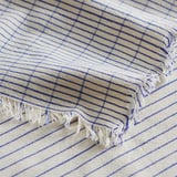 Couverture rayée beige et bleue à franges.