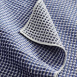 Serviette pliée en armure gaufrée bleue et blanche, présentant des motifs de losanges complexes, avec un aspect texturé et doux.