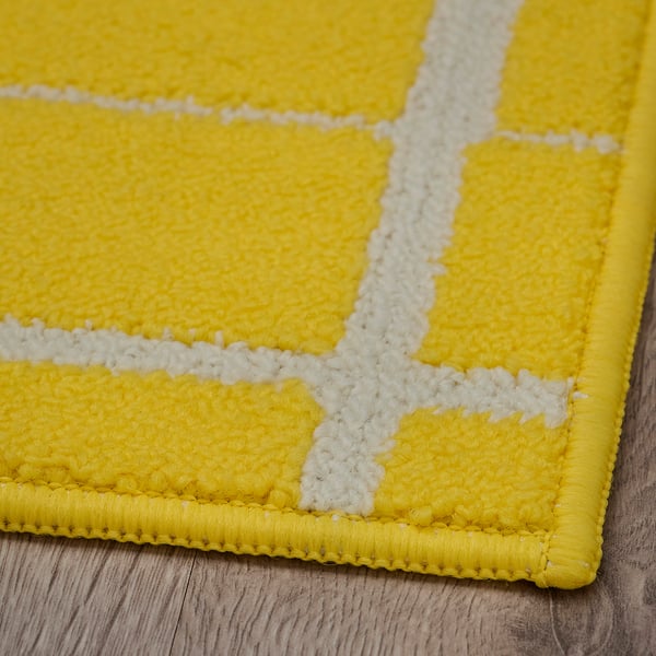 Tapis géométrique jaune vif avec des lignes blanches, exposé sur un plancher en bois. Texture douce, points réguliers, haute qualité.