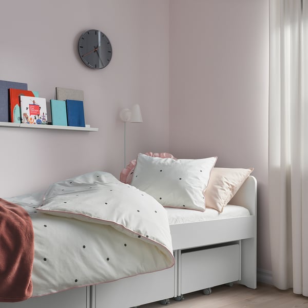 Chambre d’enfants avec literie VÄNKRETS : points blancs sur oreillers, garniture rose, horloge, livres, lampe ; Décor chaleureux.