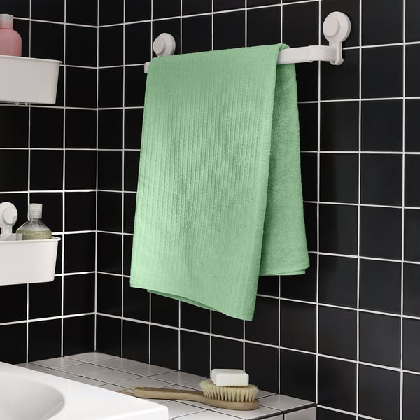 Serviette vert menthe sur support blanc contre carreaux noirs.