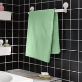 Serviette vert menthe sur support blanc contre carreaux noirs.