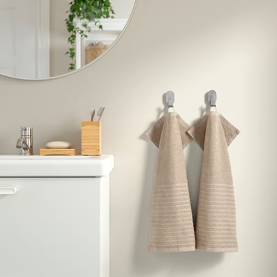 Salle de bain moderne avec serviettes beiges VÅGSJÖN suspendues, meuble-lavabo blanc, miroir rond, porte-bébé en bambou avec articles de toilette.