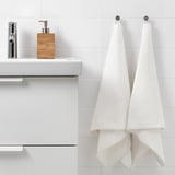 Des serviettes en coton VÅGSJÖN blanches sont suspendues à côté du lavabo de la salle de bain moderne avec distributeur de savon.