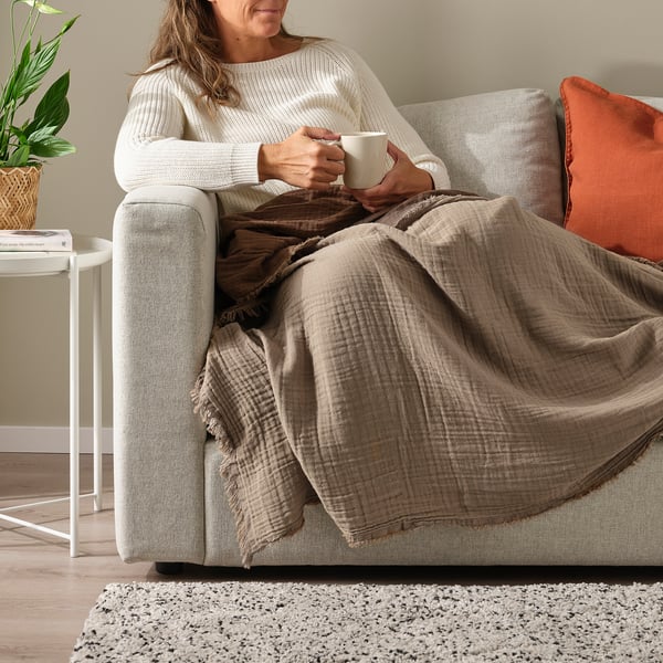 La femme se détend sur le canapé avec le plaid VALLKRASSING, profitant d’une configuration confortable.