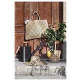 Chapeau et sac tissés en jonc de mer avec citronnier et arrosoir contre porte en bois.