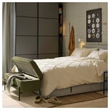 Chambre moderne avec literie blanche, pouf vert, parquet et murs gris. Œuvres d’art et cintres à proximité.