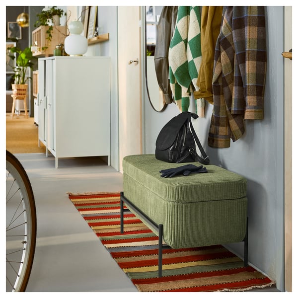 Un banc de rangement vert VALTORP dans un couloir. Il a une forme rectangulaire avec des bords surélevés et une assise rembourrée. Un sac noir et des gants sont sur le dessus.