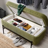 Banc rembourré vert avec pieds en métal, couvercle ouvert révélant un rangement organisé. Couvercle à charnière soutenu par des ressorts à gaz.