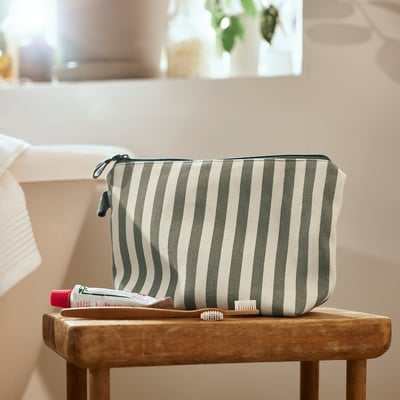 Trousse de toilette rayée verte crème sur tabouret en bois.
