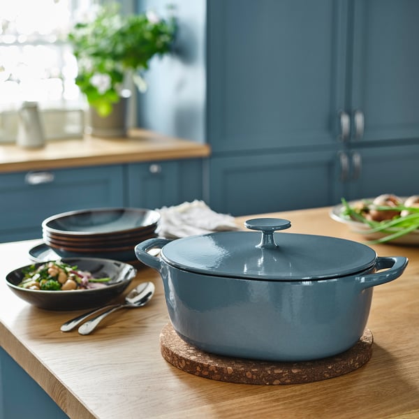 Cocotte en fonte bleue sur un comptoir en bois, avec des assiettes et un bol de salade à côté.