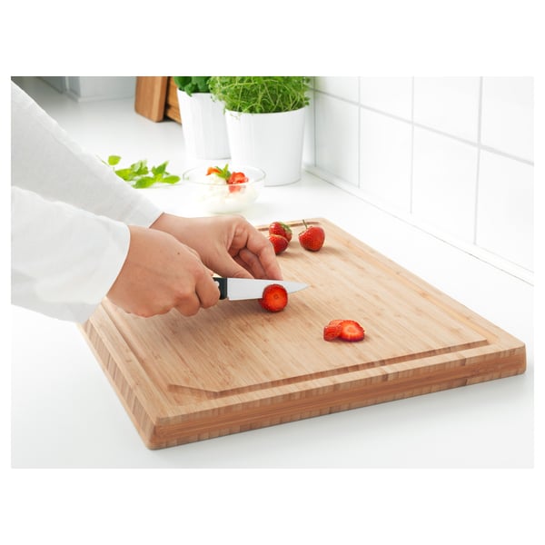La personne tranche des fraises avec un petit couteau sur une planche à découper en bois.
