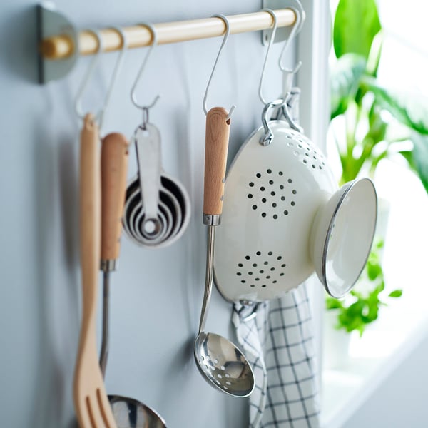Les ustensiles de cuisine, y compris une passoire et une louche, sont suspendus à des crochets, prêts à l’emploi près du poêle.
