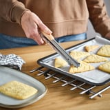 Personne utilisant une pince à épiler de cuisine pour manipuler des produits de boulangerie triangulaires sur un plateau.