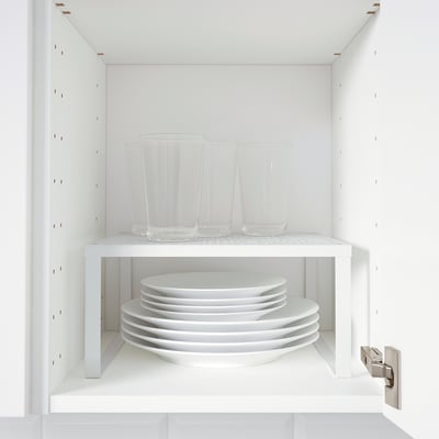 Armoire blanche avec insert d’étagère VARIERA : verres transparents sur le dessus, assiettes blanches empilées en dessous.