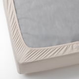 Drap de matelas en coton gris avec coins élastiques ajustés sur fond blanc cassé.