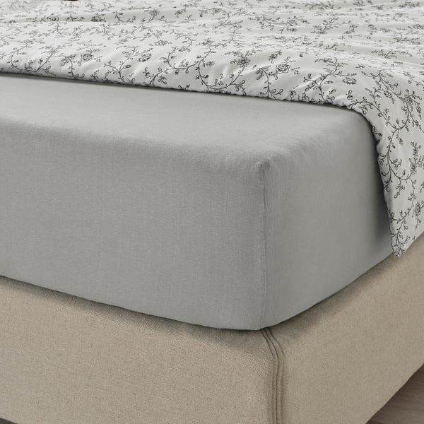 Un coin de lit avec un drap-housse en jersey de coton gris et un drap plat imprimé, montrant sa coupe douce et extensible et ses propriétés d’absorption de l’humidité.