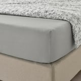 Un coin de lit avec un drap-housse en jersey de coton gris et un drap plat imprimé, montrant sa coupe douce et extensible et ses propriétés d’absorption de l’humidité.