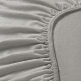 Gros plan sur un tissu jersey doux et extensible sur le drap de lit, mettant en valeur les détails des bords élastiques.