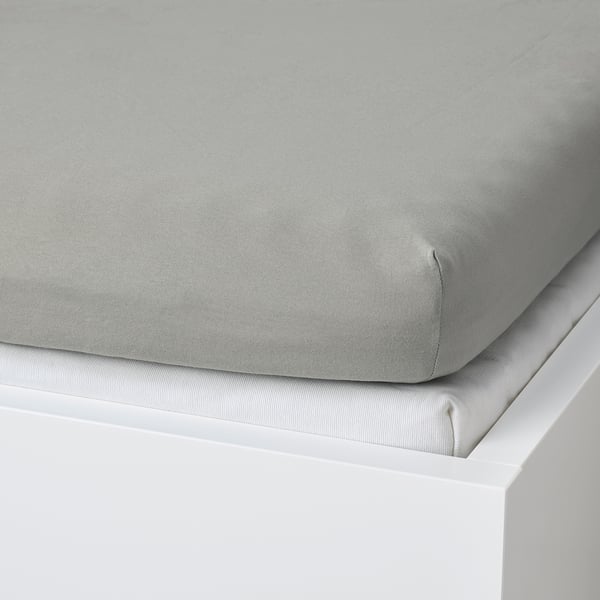 Drap-housse gris sur lit blanc, mettant en valeur son coin élastique pour un ajustement sûr.