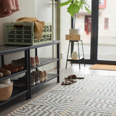Entrée avec boîte VEDKLYV verte sur étagère à chaussures, près de l’usine et de la porte.