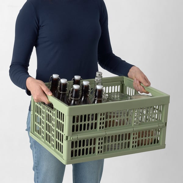 Personne portant une caisse en plastique vert remplie de bouteilles.