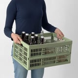 Personne portant une caisse en plastique vert remplie de bouteilles.