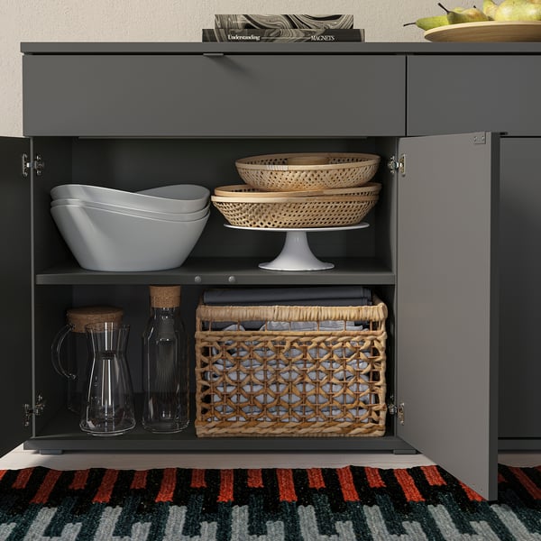 Armoire grise avec deux sections ouvertes. Le dessus contient des bols empilés. Le fond contient des bocaux et un panier avec des chiffons.