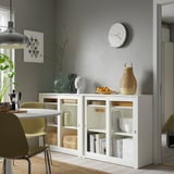 Salle à manger moderne avec armoire VIHALS blanche, portes vitrées et design élégant, s’adaptant entre les chaises et près d’un mur gris.