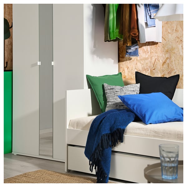 Coin chambre confortable avec lit de repos ikea VIHALS blanc, oreillers et couverture bleus, et placard avec des vêtements colorés.