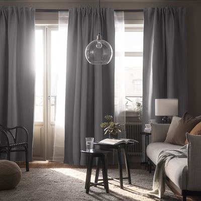 Chambre moderne avec rideaux gris VILBORG, lumière douce, canapé gris et tabouret noir.