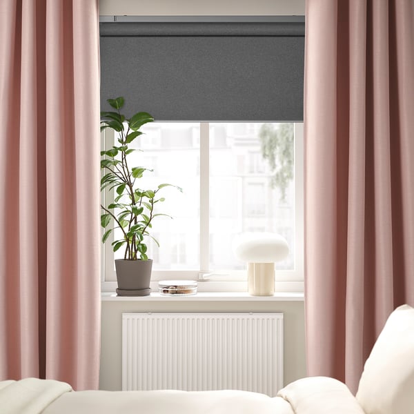 Chambre moderne avec des rideaux roses VILBORG, élégante, longue au sol, bloquant doucement la lumière. Plante en pot, lampe et radiateur blanc sous une grande fenêtre.